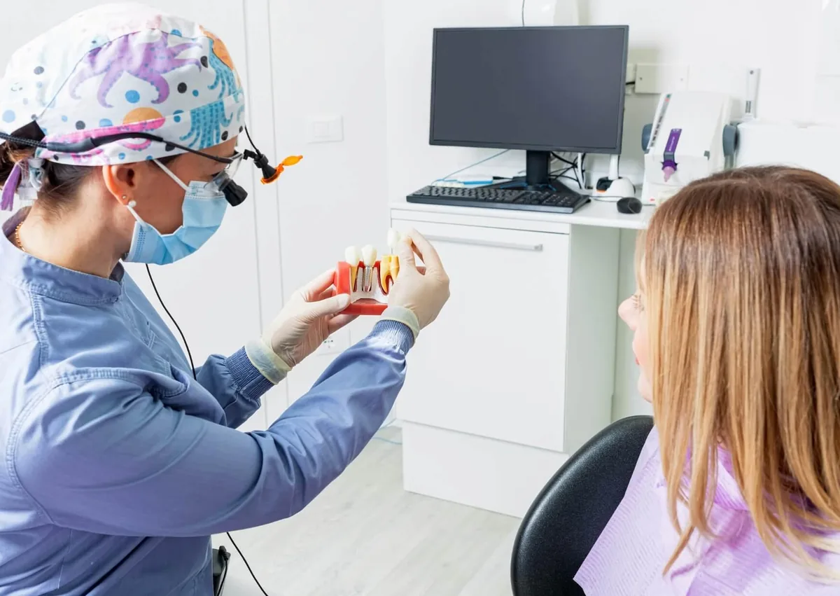 Dentist showing a patient a dental implant model while discussing implant lifespan and long-term care.