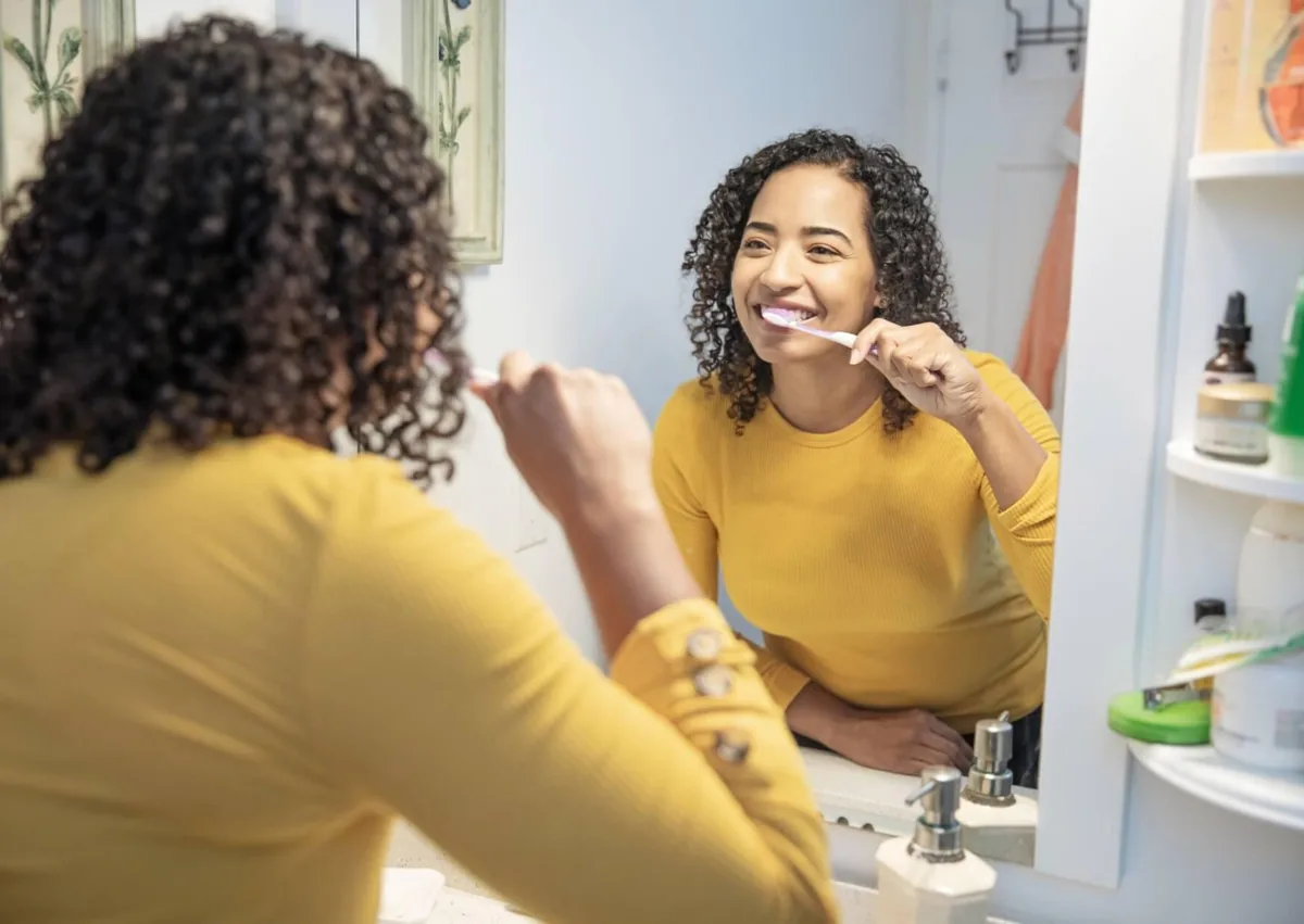 Woman brushing her teeth at home as part of a daily preventive dental care routine.